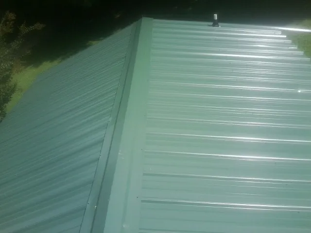 New green metal panels meeting at the ridge of a roof — Flat Roof Repair work by our crew in Wedgefield