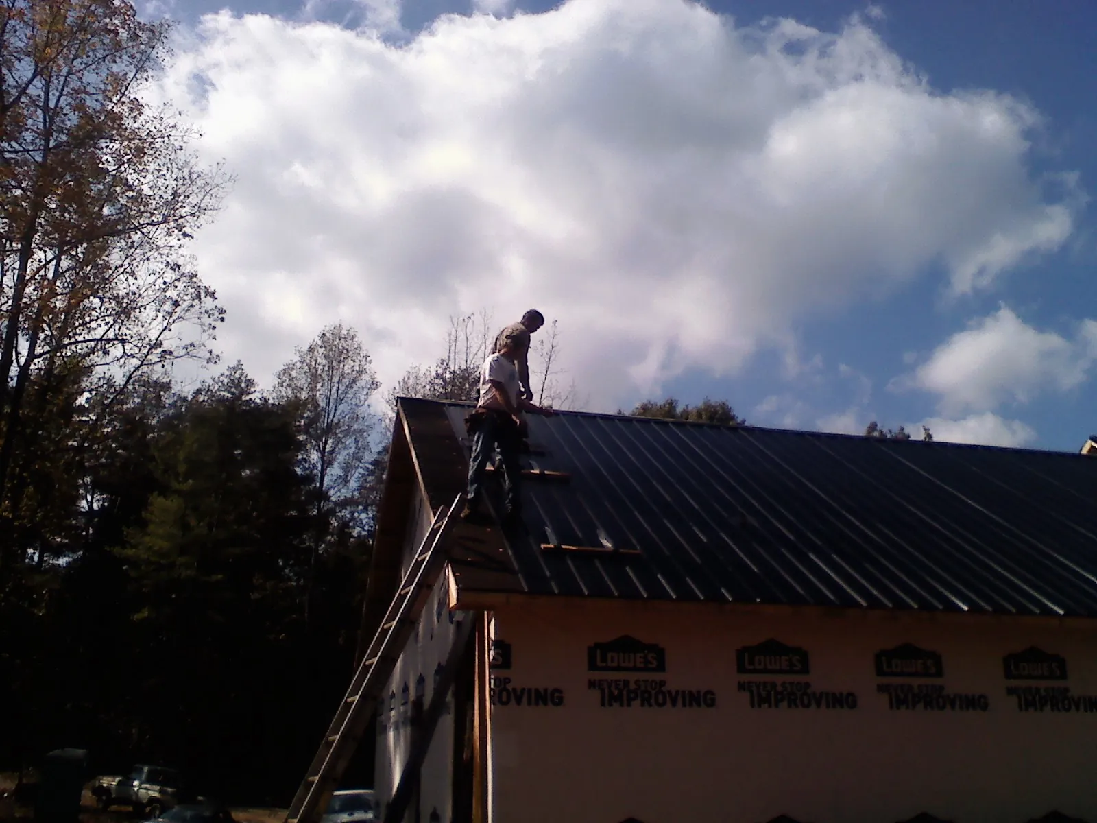 Roofer fastening dark metal panels high against a cloudy sky, from a Roof Inspection job in Wedgefield
